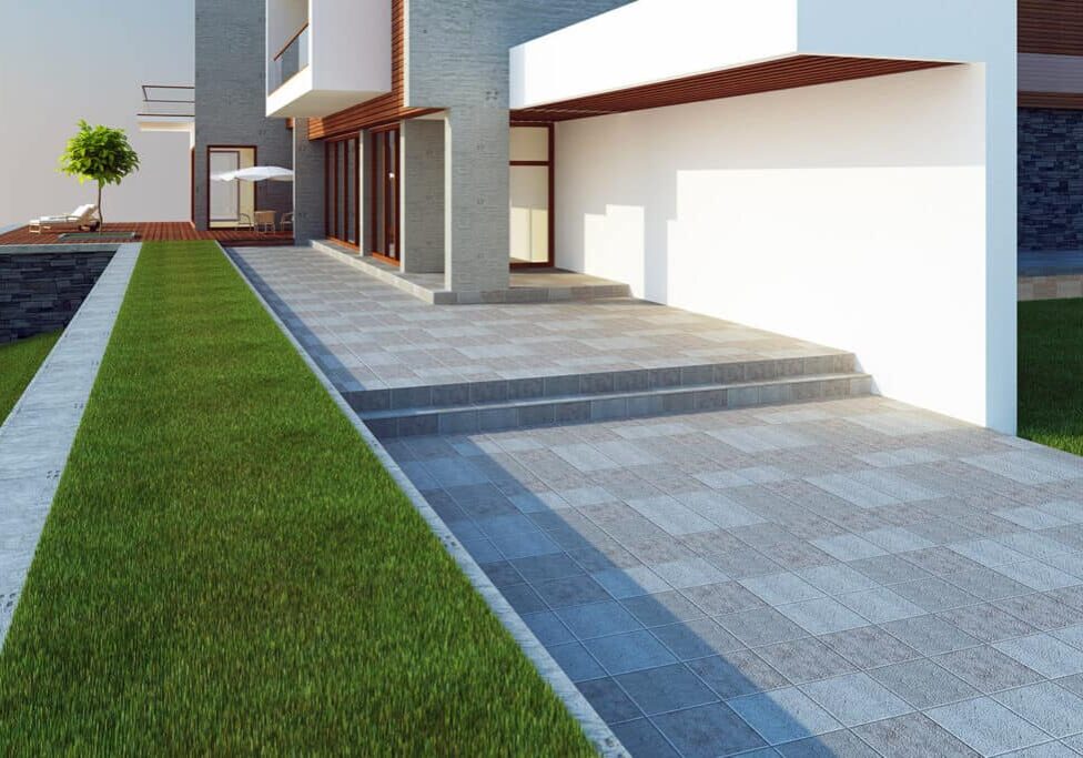 Modern house with large windows, white walls, and gray stone accents. A paved driveway with steps leads to the entrance, bordered by neatly trimmed green grass and a retaining wall crafted by expert Seattle Landscaping.